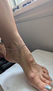 Close-up of a foot with a anklet on a white surface.